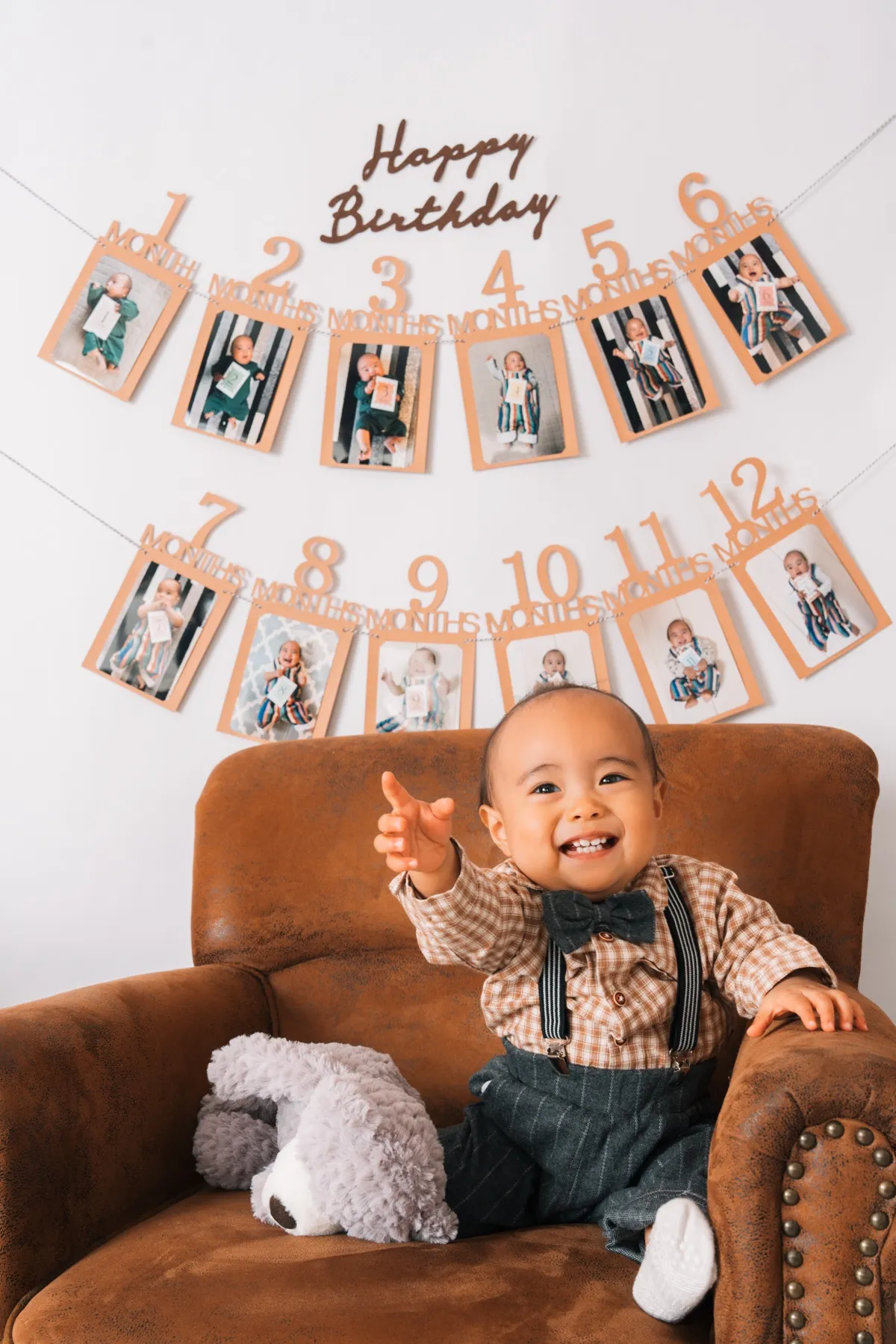 12ヶ月の成長記録ガーランドの前で、ソファに座って笑う1歳の男の子